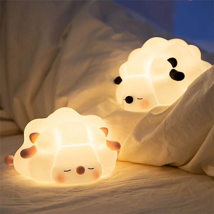 Two sheep-shaped night lights on a bed with a soft focus background
